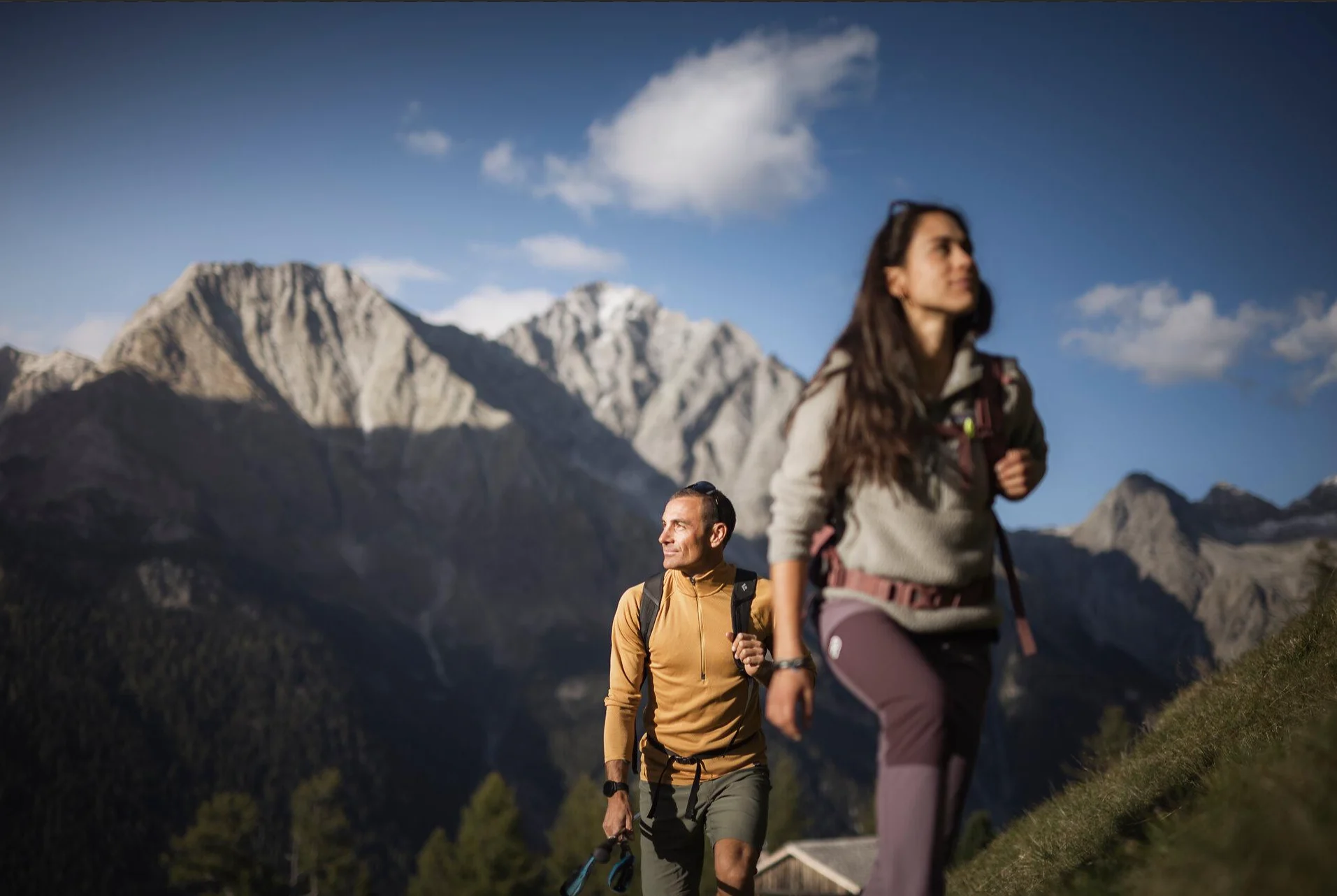 Zwei Wanderer auf einem Bergpfad vor sonnigen Berggipfeln